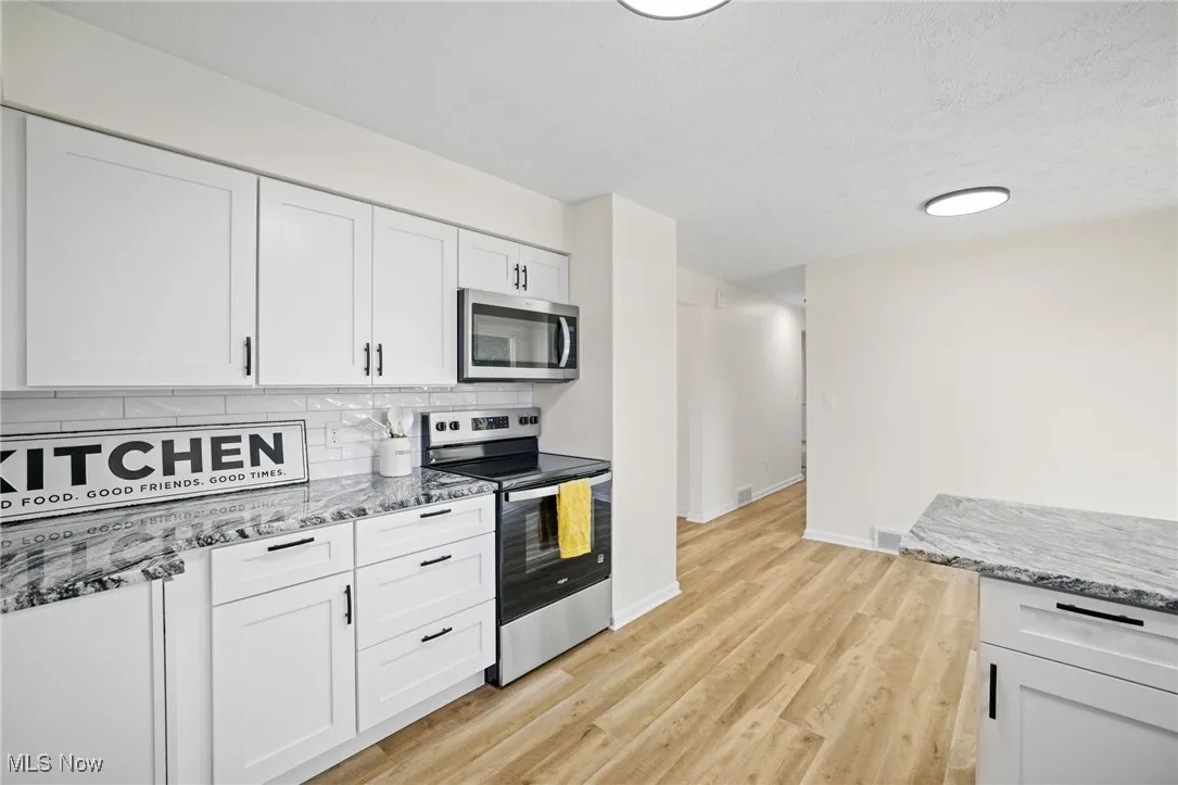Kitchen featuring stainless steel appliances, decorative backsplash, white cabinets, light stone countertops, and light wood-type flooring