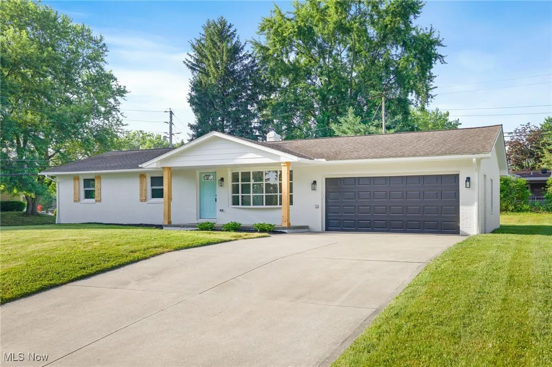 Ranch-style home featuring an attached garage, concrete driveway, a front lawn, and covered porch