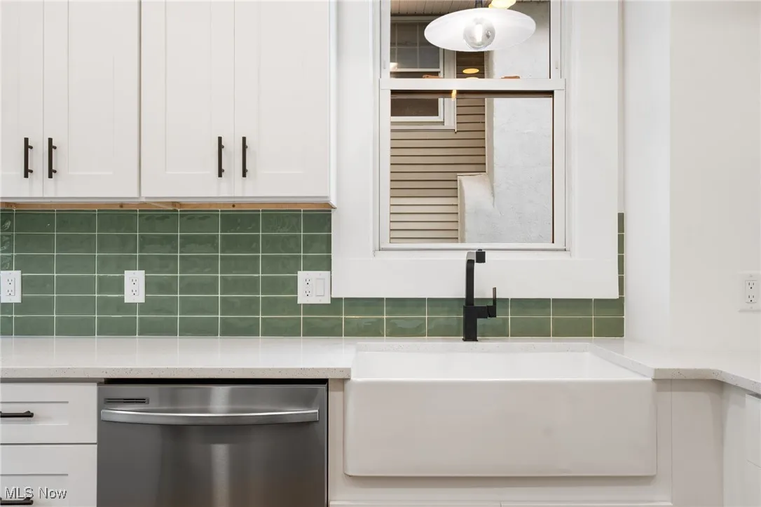 Kitchen with dishwasher, white cabinets, backsplash, and light stone counters