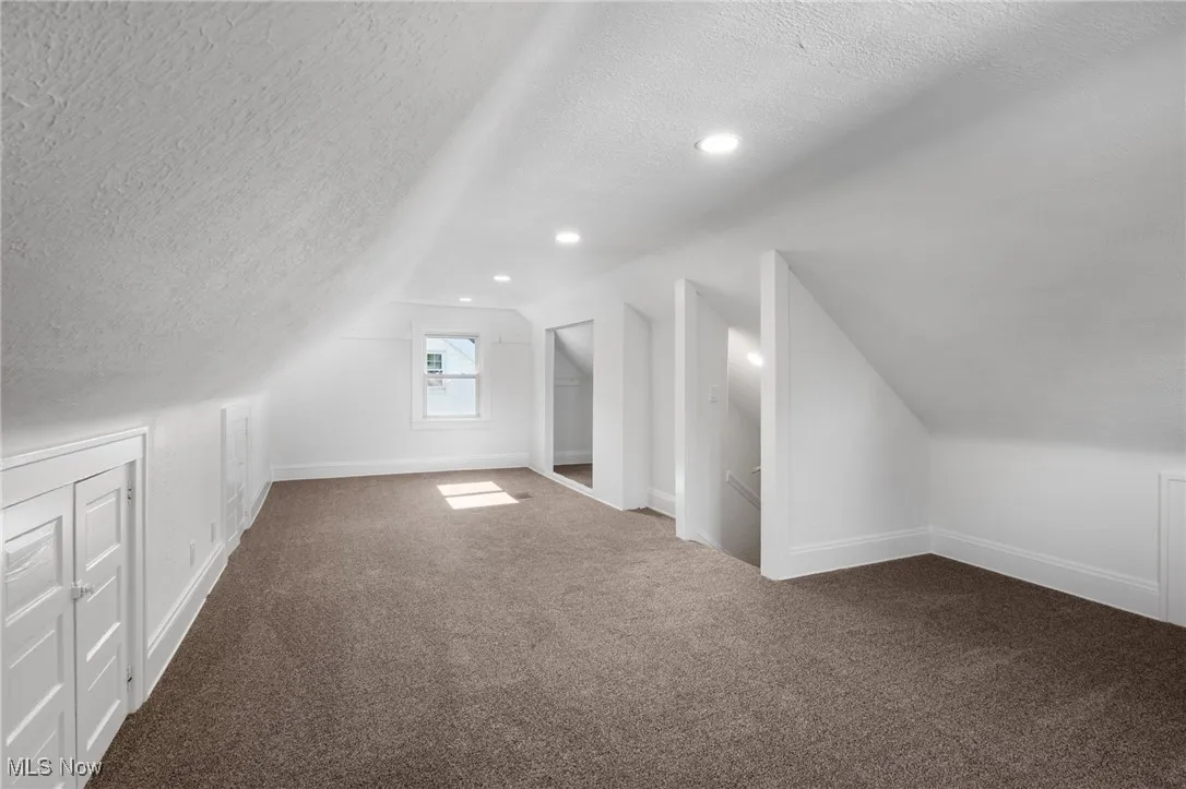 Bonus room featuring a textured ceiling, dark colored carpet, lofted ceiling, and recessed lighting