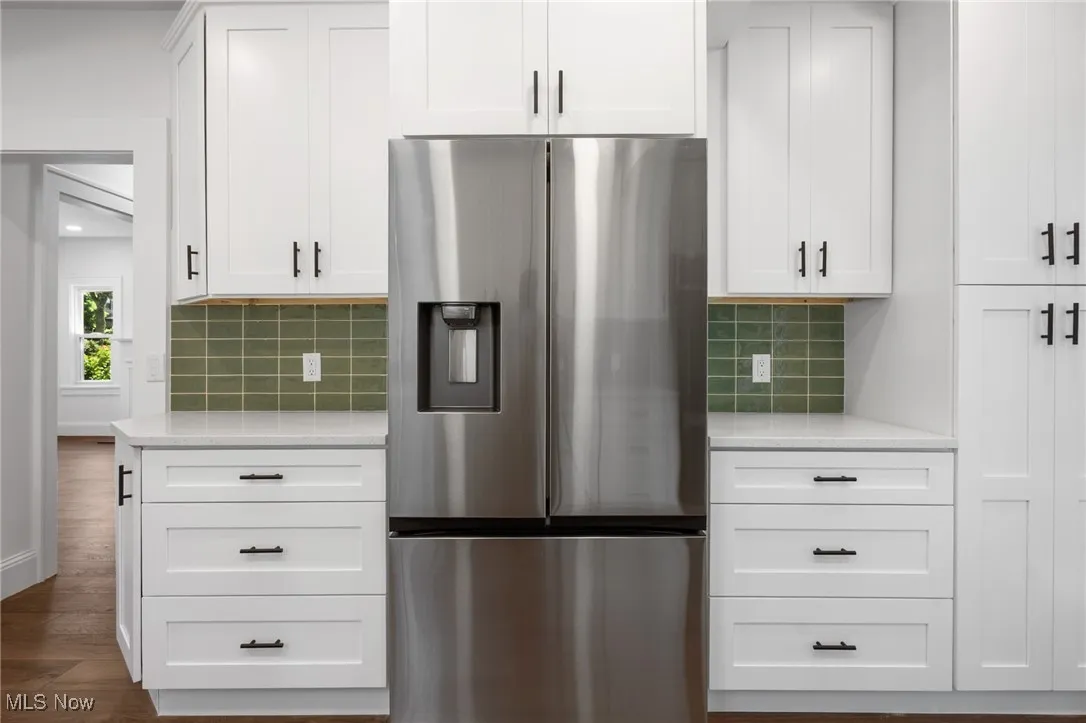 Kitchen with stainless steel fridge, light countertops, dark wood-type flooring, and tasteful backsplash
