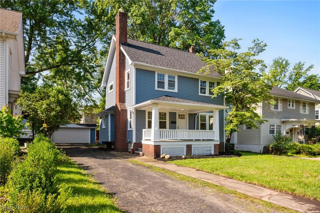 Traditional style home featuring a chimney, a porch, a front lawn, an outbuilding, and a detached garage
