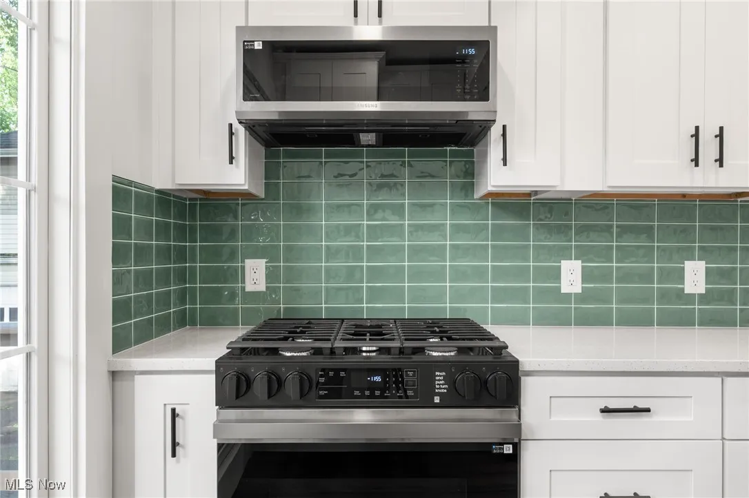 Kitchen with gas stove, stainless steel microwave, white cabinets, backsplash, and light stone counters