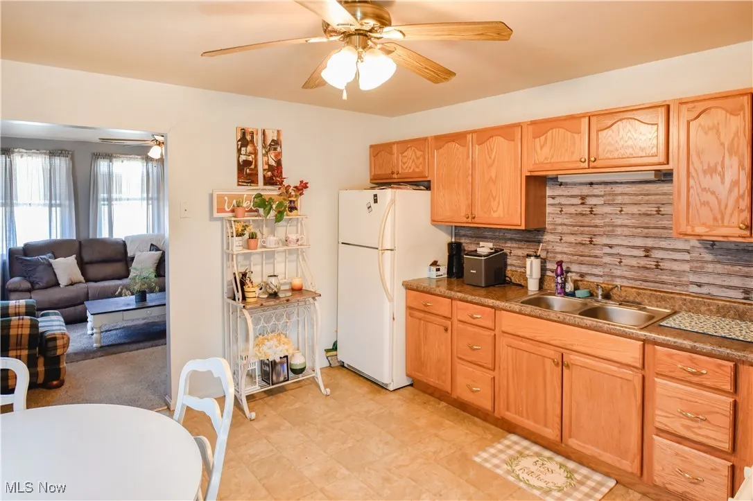 Kitchen featuring freestanding refrigerator, ceiling fan, light brown cabinets, and backsplash
