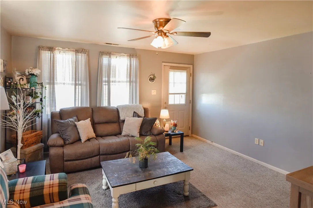 Carpeted living area with ceiling fan and baseboards