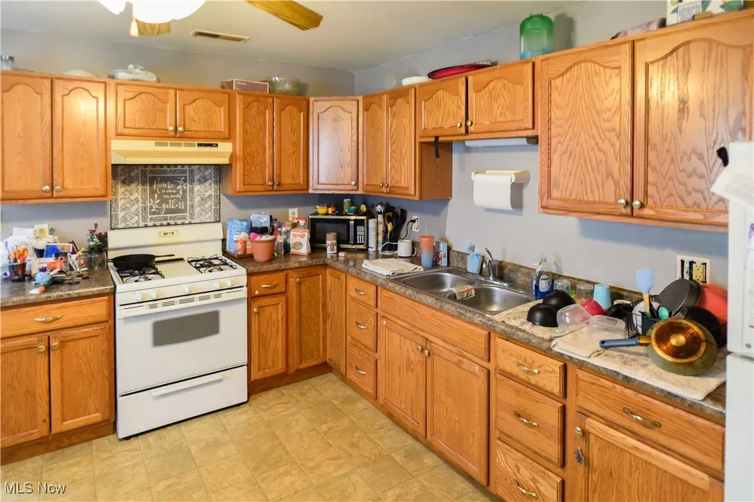 Kitchen featuring white range with gas cooktop, under cabinet range hood, stainless steel microwave, ceiling fan, and brown cabinets