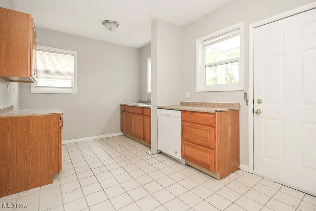 Kitchen with dishwasher, light countertops, brown cabinets, and light tile patterned floors