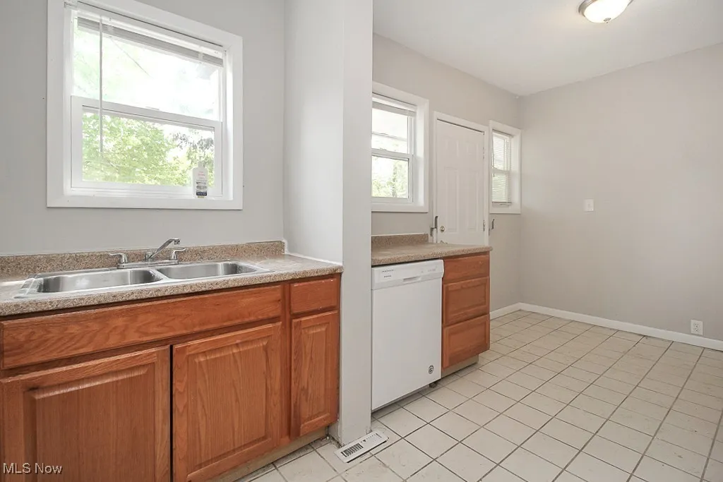 Kitchen with white dishwasher, light countertops, brown cabinets, and light tile patterned flooring