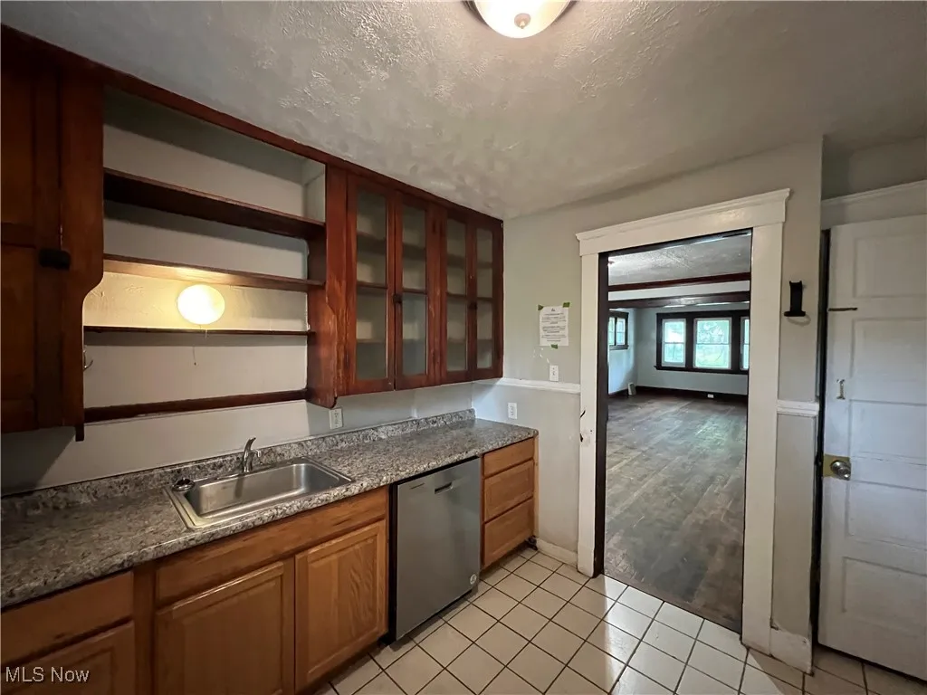 Kitchen with stainless steel dishwasher, a textured ceiling, open shelves, light tile patterned floors, and glass insert cabinets
