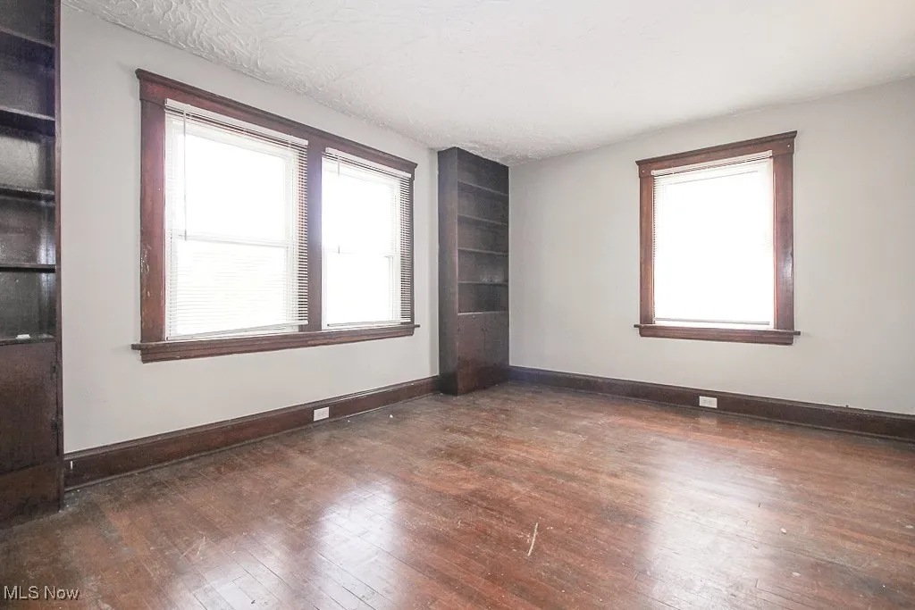 Unfurnished room with hardwood / wood-style flooring, built in shelves, and a textured ceiling