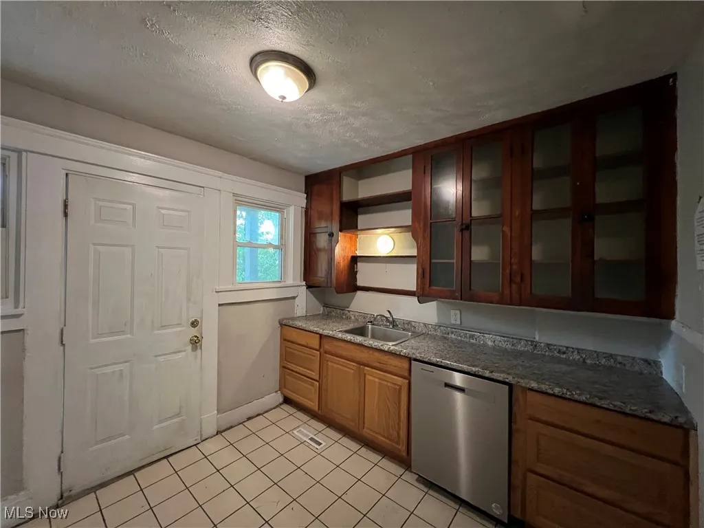 Kitchen featuring dishwasher, a textured ceiling, open shelves, light tile patterned flooring, and glass insert cabinets