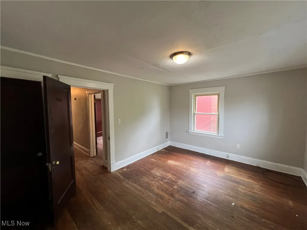 Empty room featuring dark wood finished floors and ornamental molding