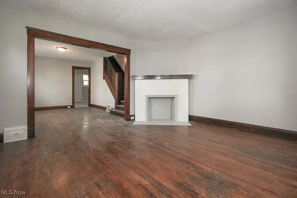 Unfurnished living room featuring hardwood / wood-style flooring, stairway, and a fireplace with flush hearth