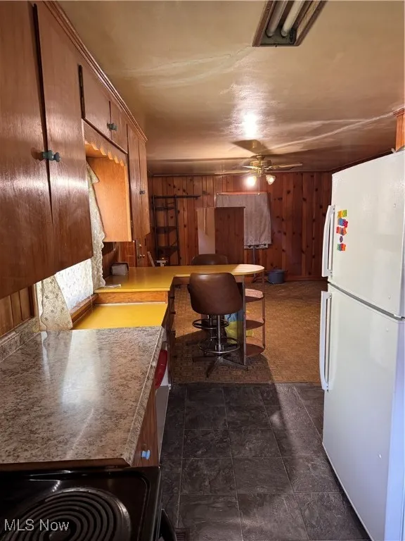 Kitchen featuring fridge, a ceiling fan, brown cabinets, range, and wood walls