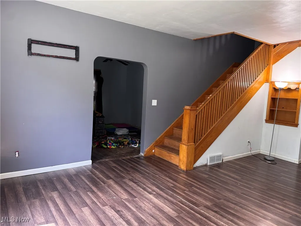 Unfurnished living room featuring wood finished floors, stairway, and arched walkways