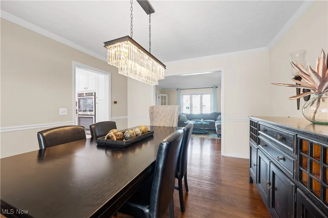 Dining area with a chandelier, ornamental molding, and dark wood-style flooring