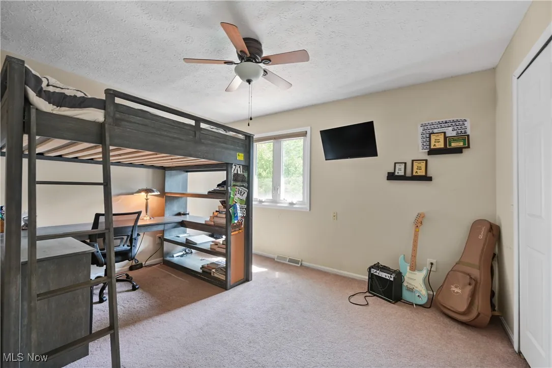 Carpeted bedroom with a desk, a textured ceiling, and ceiling fan