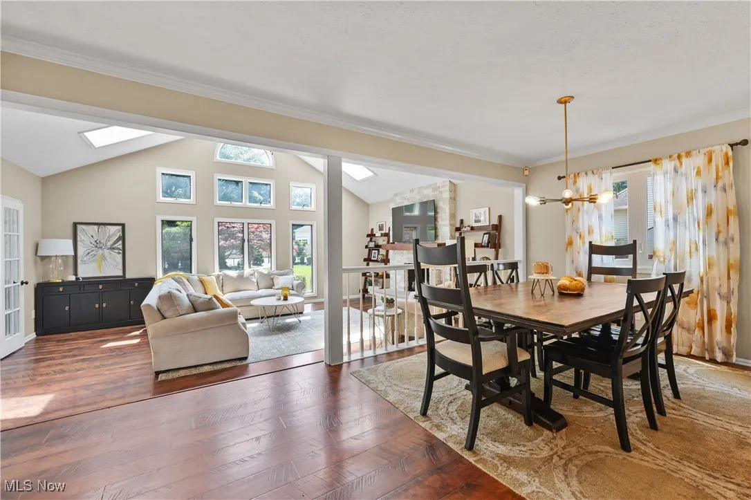 Dining space featuring vaulted ceiling, dark wood-style floors, ornamental molding, a chandelier, and a skylight