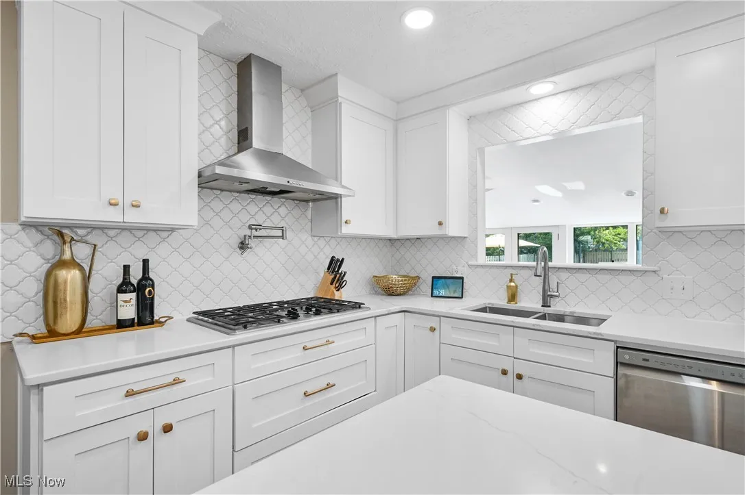 Kitchen with stainless steel appliances, wall chimney exhaust hood, white cabinetry, backsplash, and recessed lighting