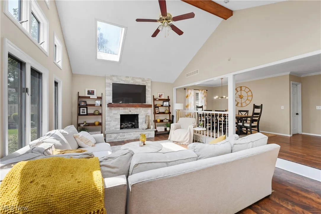 Living room featuring high vaulted ceiling, ceiling fan, plenty of natural light, a fireplace, and beam ceiling