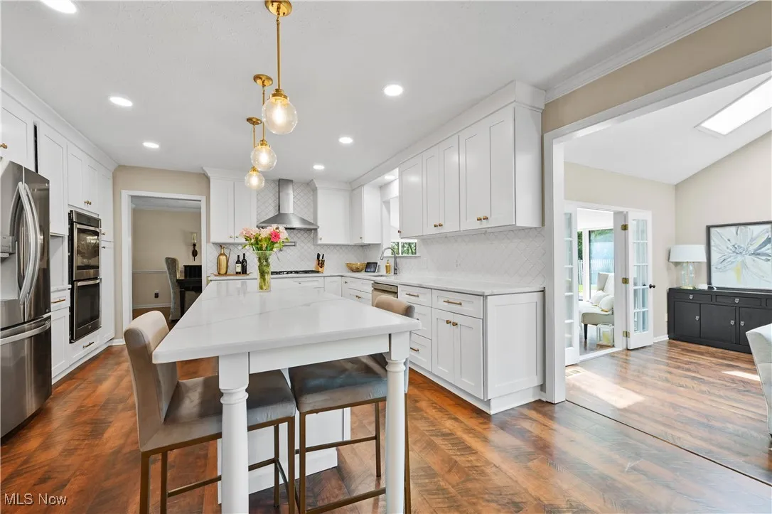 Kitchen featuring stainless steel appliances, wall chimney range hood, backsplash, white cabinetry, and recessed lighting