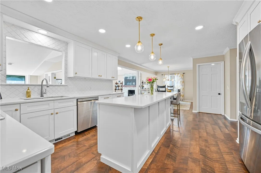 Kitchen with appliances with stainless steel finishes, decorative backsplash, ornamental molding, light countertops, and white cabinetry