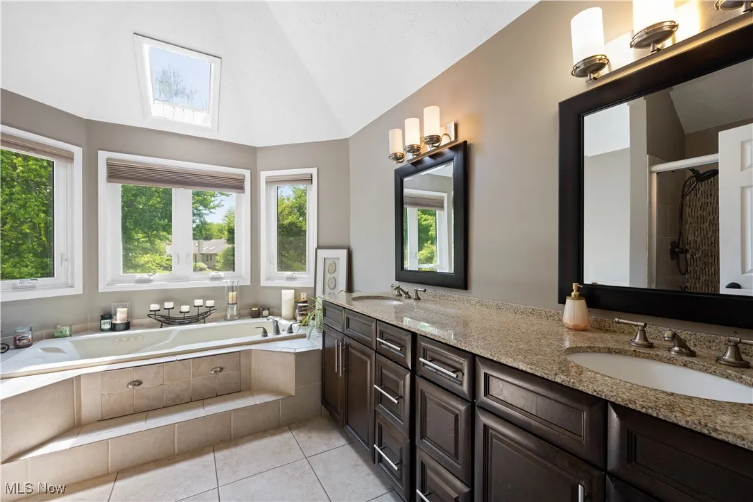 Bathroom featuring double vanity, lofted ceiling, a bath, tile patterned floors, and a stall shower