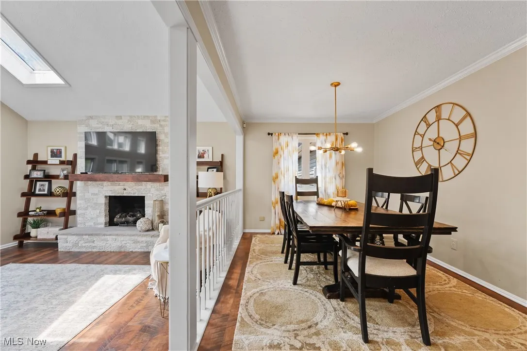 Dining area with wood finished floors, a chandelier, a skylight, a stone fireplace, and crown molding