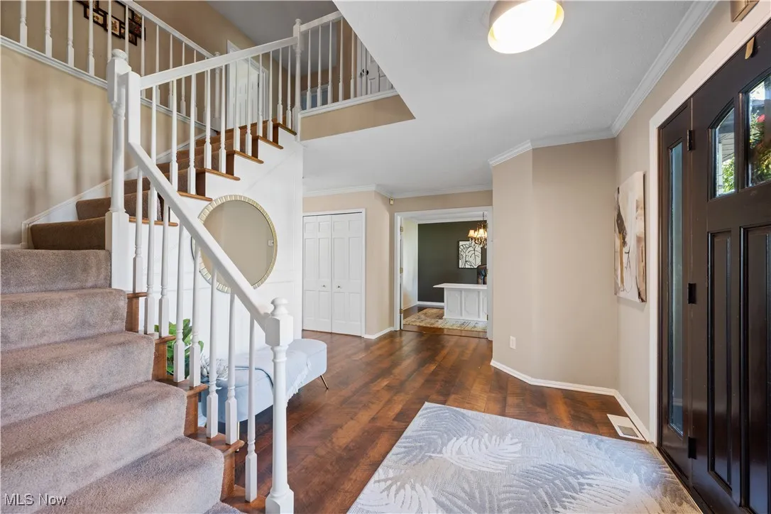 Foyer with wood finished floors, stairway, crown molding, and a chandelier