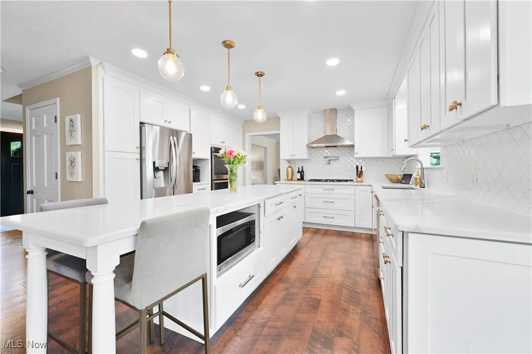 Kitchen featuring wall chimney range hood, appliances with stainless steel finishes, decorative backsplash, a kitchen island, and recessed lighting