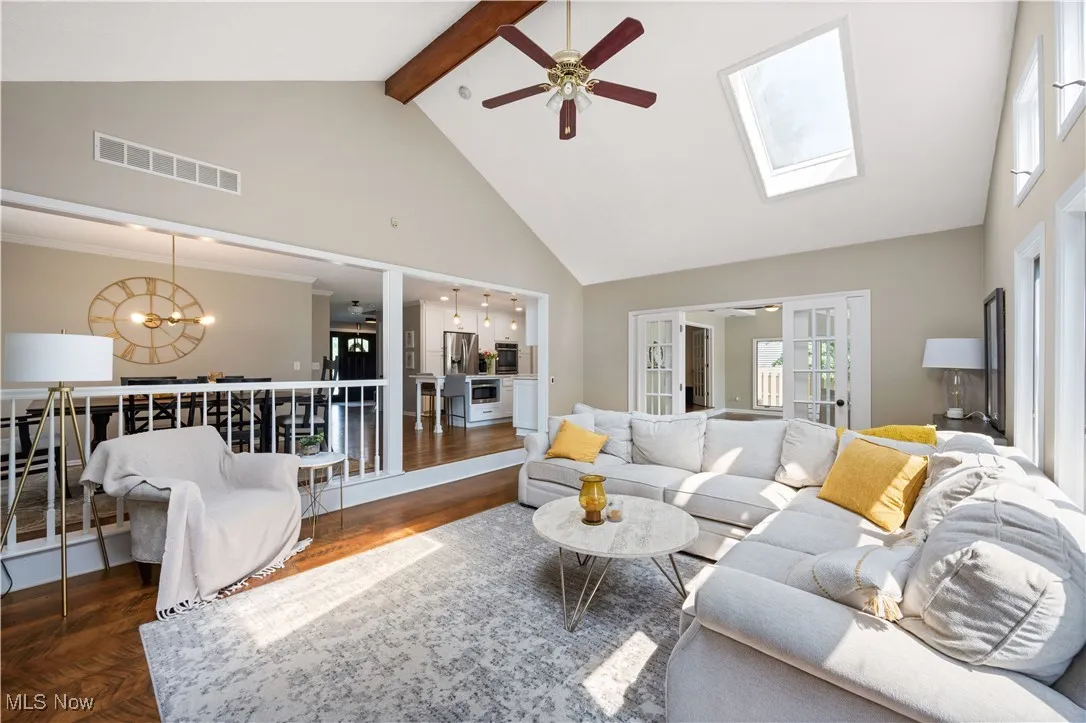 Living room with high vaulted ceiling, a ceiling fan, a chandelier, beamed ceiling, and a skylight