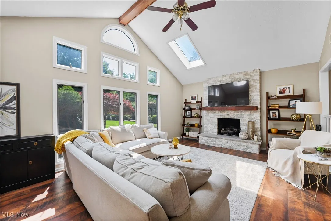 Living area featuring a ceiling fan, a skylight, dark wood-type flooring, high vaulted ceiling, and a fireplace