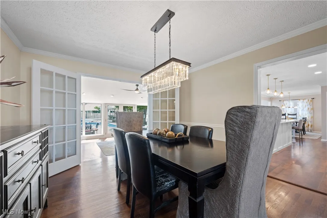 Dining area with a chandelier, a textured ceiling, dark wood-style flooring, crown molding, and ceiling fan