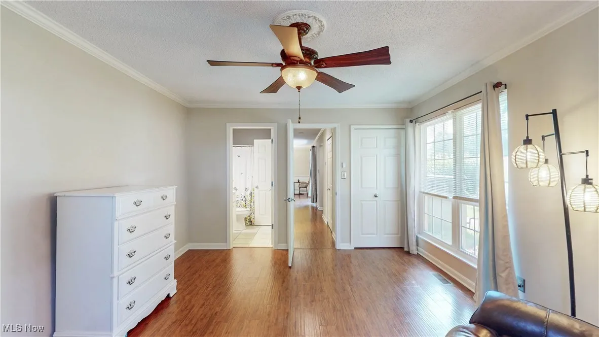 Bedroom featuring wood finished floors, a textured ceiling, crown molding, ceiling fan, and ensuite bath