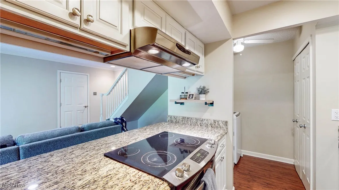 Kitchen featuring stove, exhaust hood, a ceiling fan, dark wood finished floors, and light stone countertops