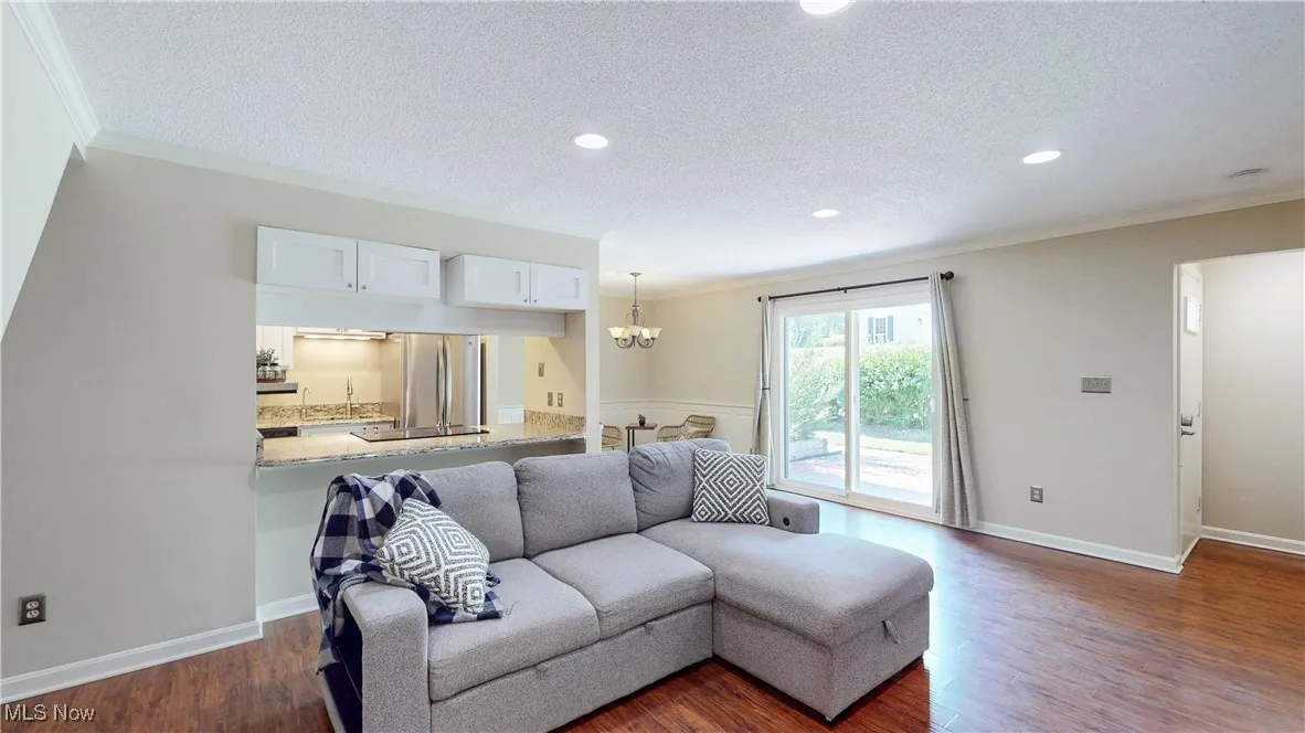 Living room featuring a textured ceiling, crown molding, a chandelier, dark wood-style floors, and recessed lighting