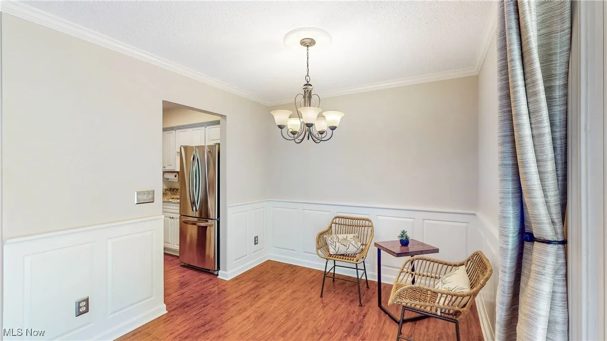Living area featuring a chandelier, ornamental molding, wood finished floors, a wainscoted wall, and a decorative wall
