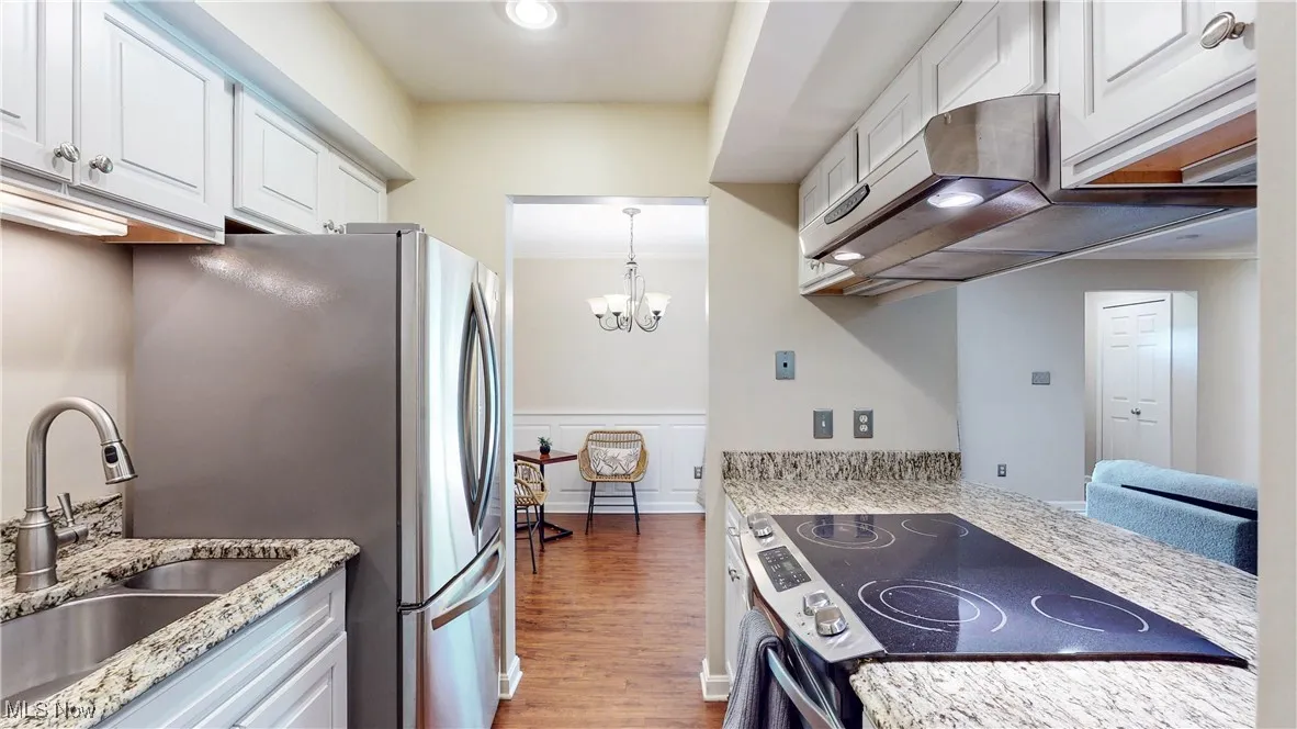 Kitchen with stainless steel appliances, exhaust hood, wood finished floors, white cabinetry, and light stone counters