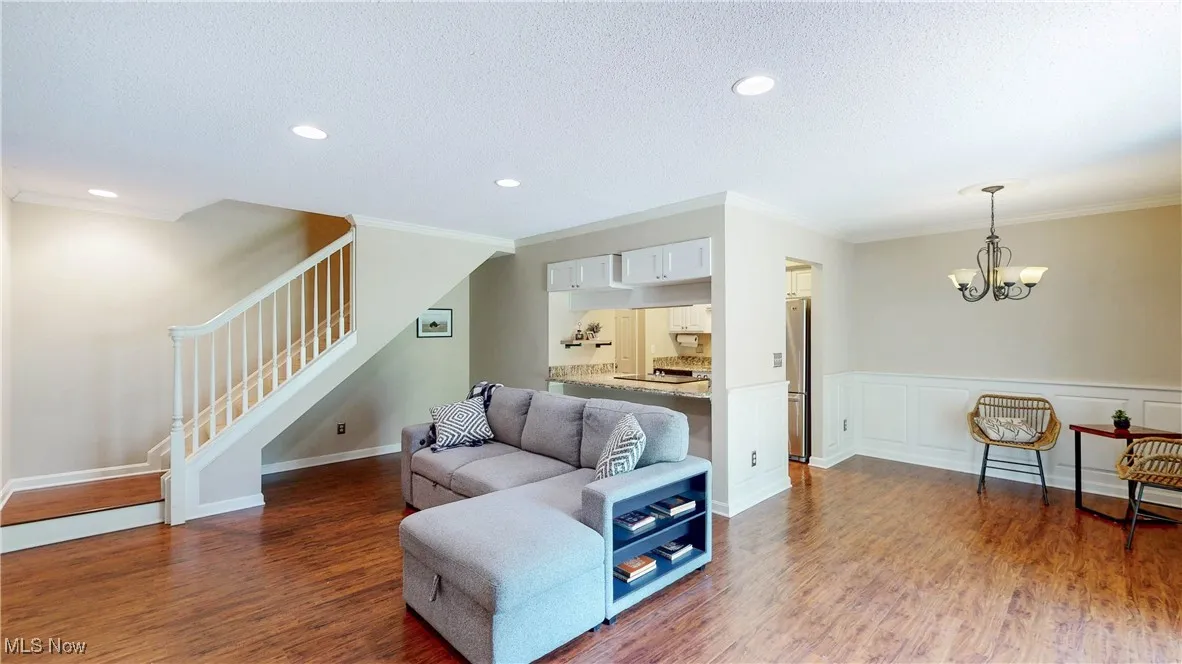 Living area with stairs, wood finished floors, a chandelier, ornamental molding, and a wainscoted wall