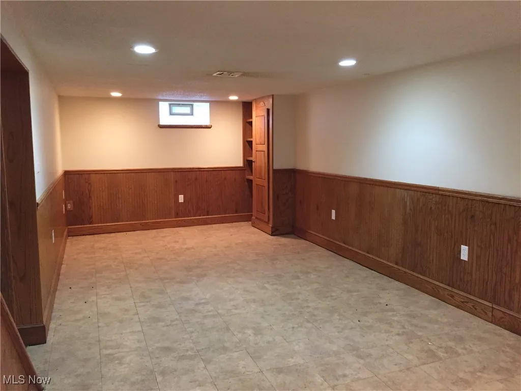 Basement featuring a wainscoted wall, wooden walls, recessed lighting, and light flooring