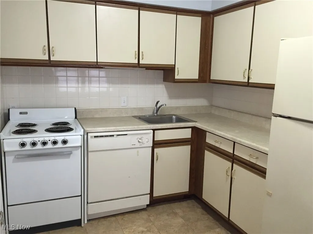 Kitchen featuring white appliances, light countertops, backsplash, and white cabinetry