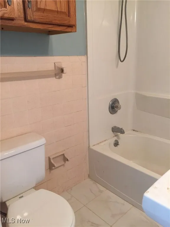 Full bathroom featuring tile walls, shower / tub combination, wainscoting, and marble look tile flooring