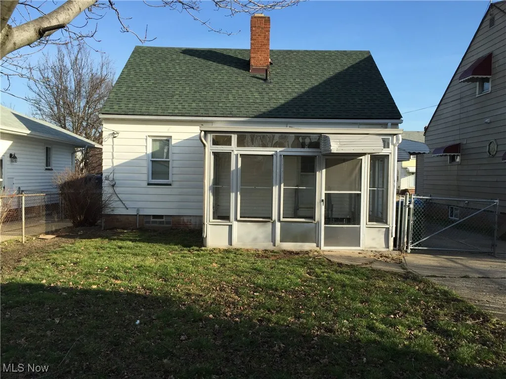Back of house with a sunroom, a shingled roof, a chimney, and a gate