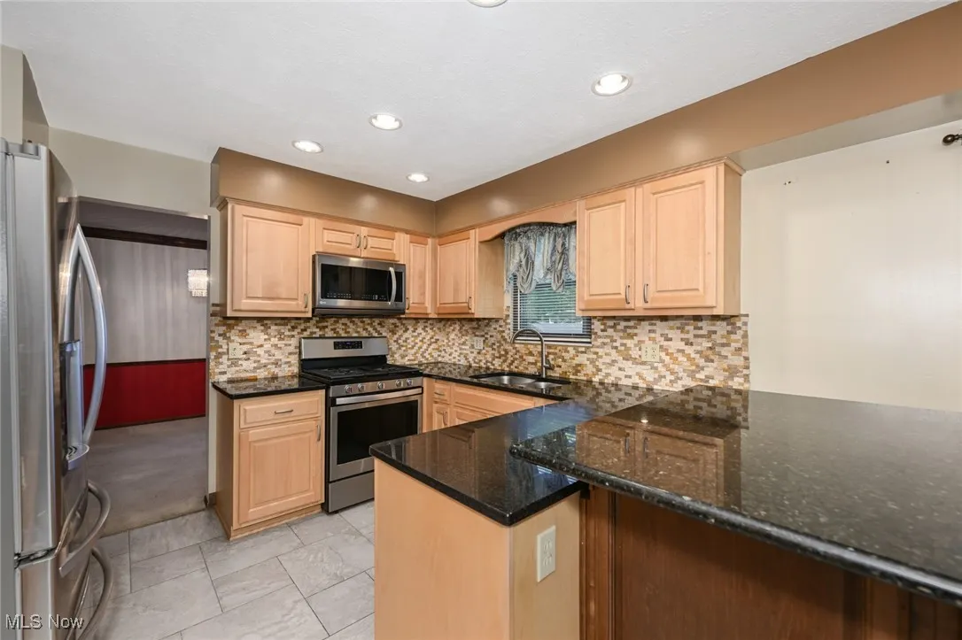 Kitchen with stainless steel appliances, light brown cabinets, backsplash, granite countertops, and recessed lighting