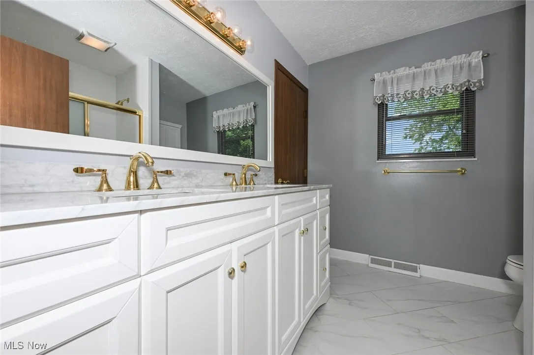 Full bath with double vanity, marble finish floors, a stall shower, and a textured ceiling