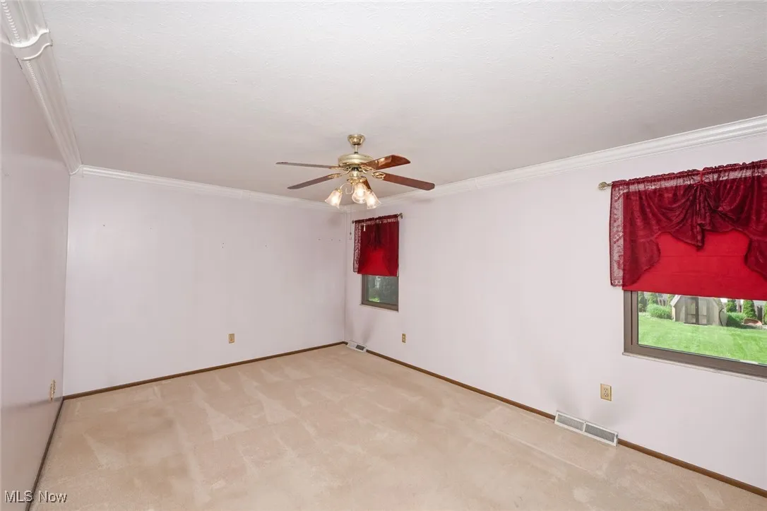 Carpeted primary bedroom featuring ceiling fan and ornamental molding