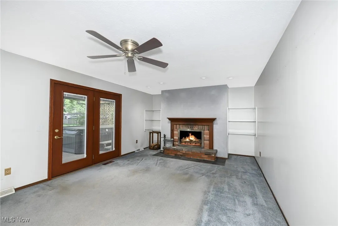 Featuring a fireplace, ceiling fan, carpet, and french doors leading to deck