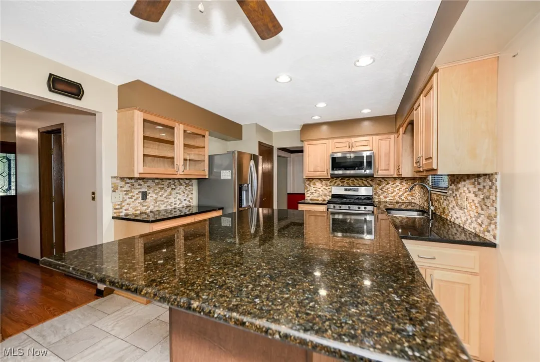 Kitchen featuring stainless steel appliances, ceiling fan, glass insert cabinets, a dining area, and light brown cabinets