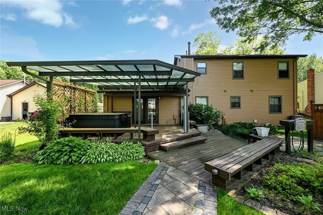 Rear view of house with a hot tub, a deck, and paved patio
