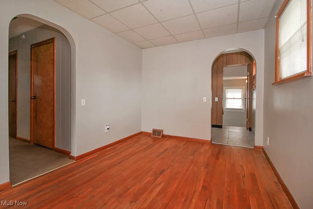 Empty room featuring arched walkways, a paneled ceiling, and wood finished floors